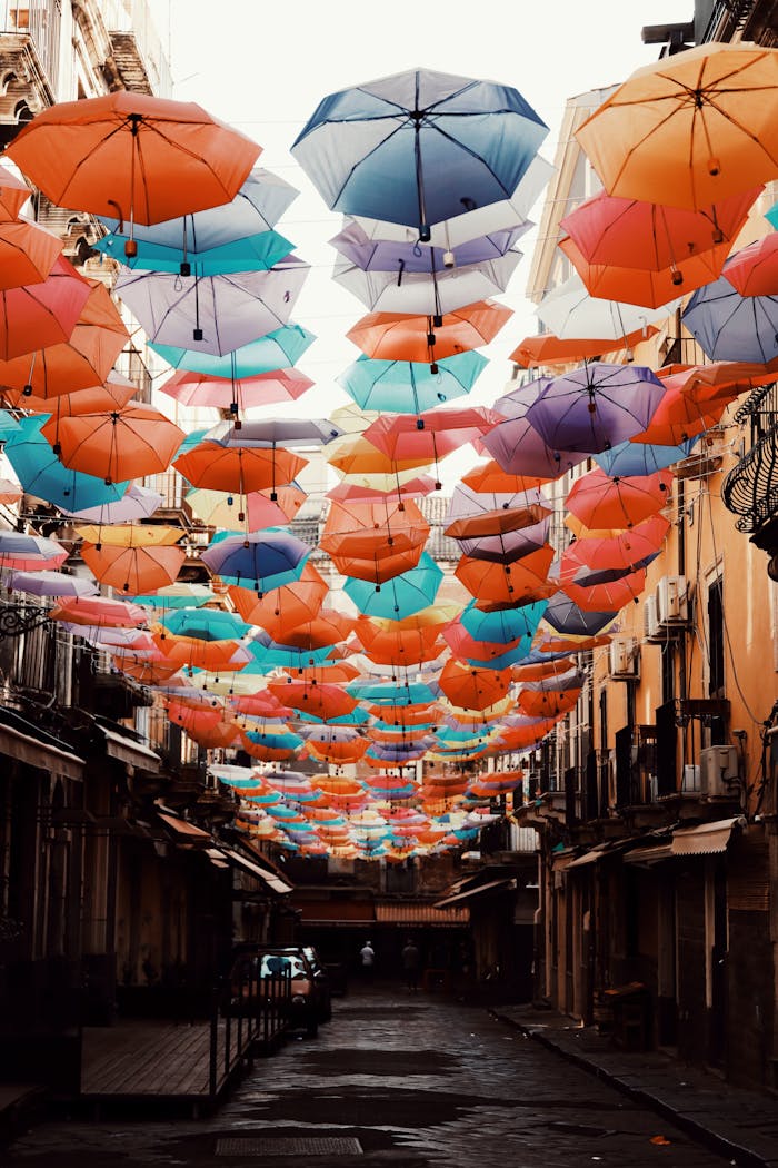 Vibrant umbrellas hang over a charming alley in Catania, Sicily, Italy, creating a lively urban scene.