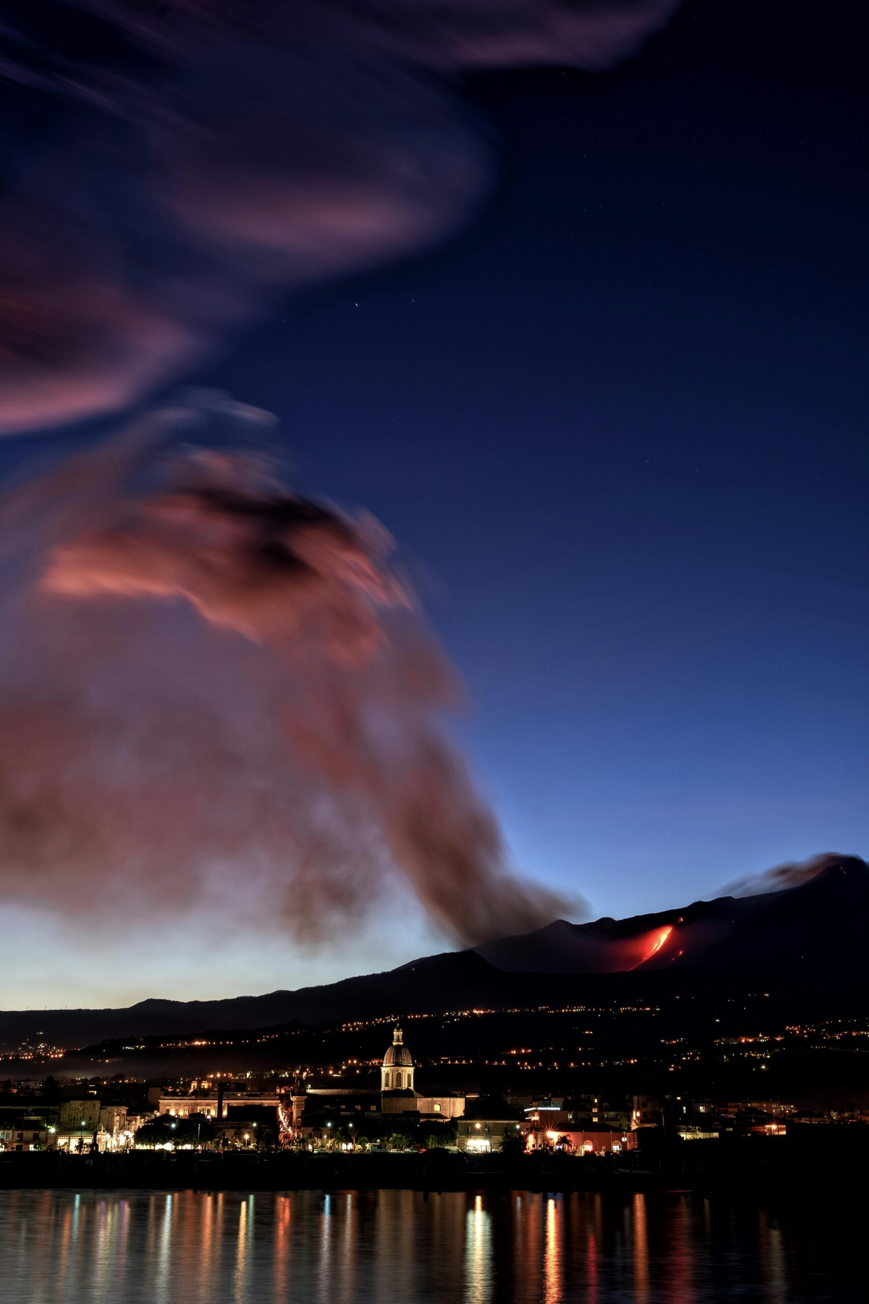 Captivating night view of Mount Etna erupting in Sicily, Italy, with glowing lava and city lights.