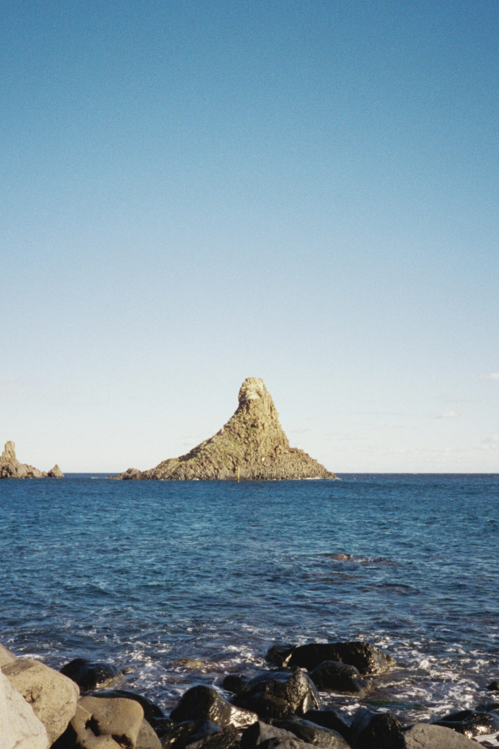 Beautiful coastal view of Cyclopean Isles off Sicily's coast, with clear blue skies.